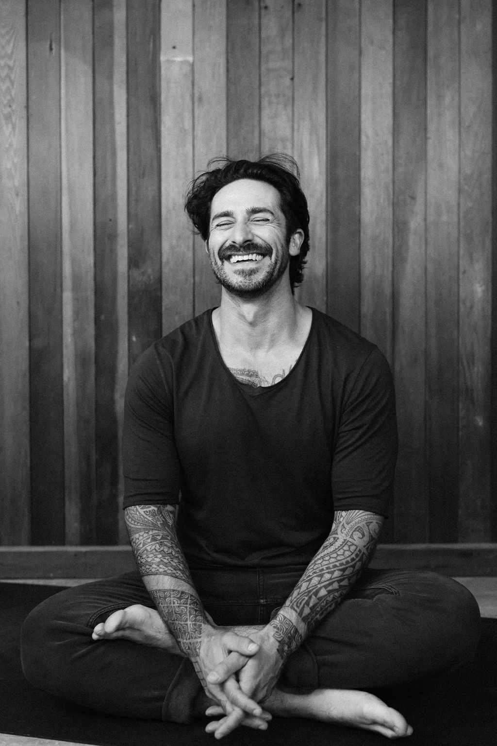 Peter Walters, laughing while seated in front of a wooden wall